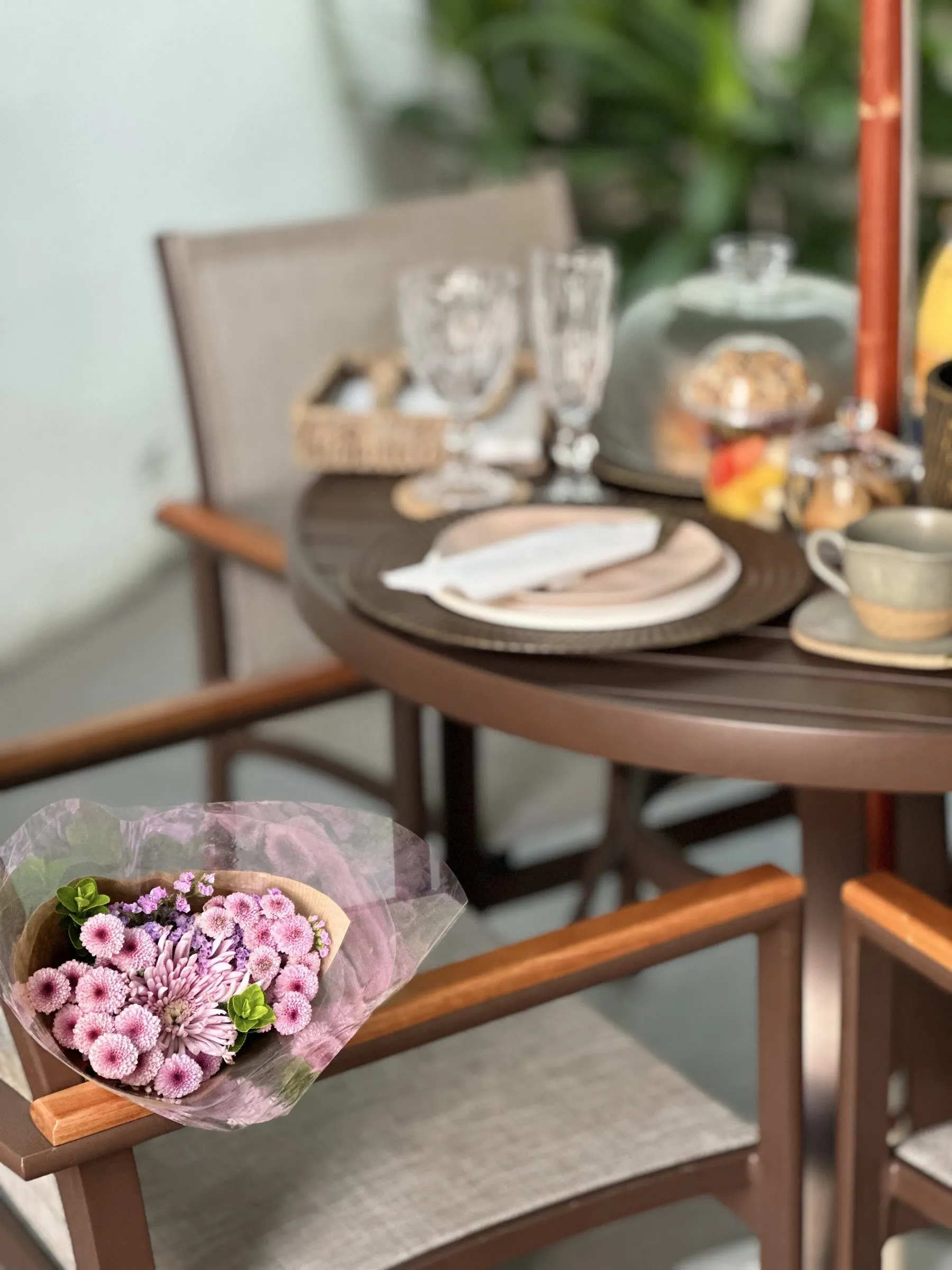 Mesa de brunch com um buquê de flores cor-de-rosa, frutas, granola, taças e xícaras da casa