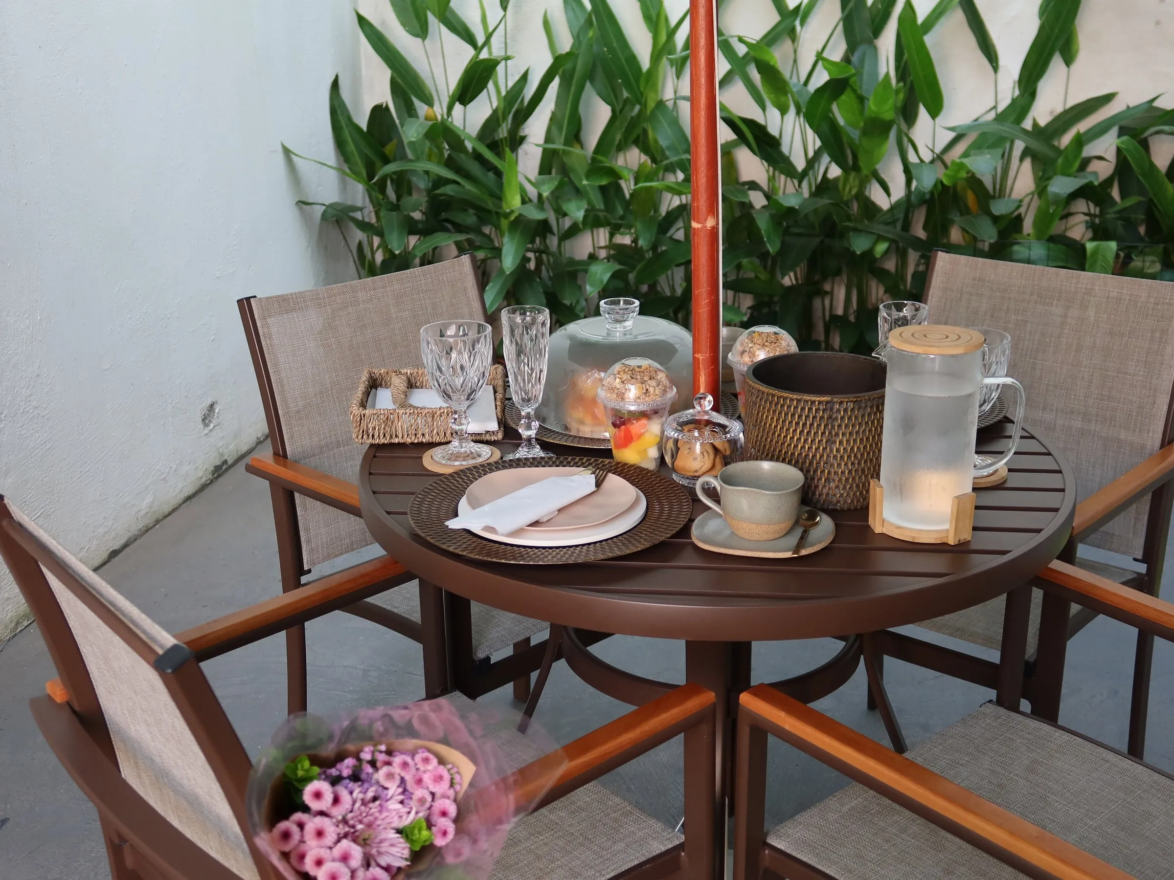 Mesa de brunch no jardim da Casa Yahava, com frutas, sucos e um buquê de flores