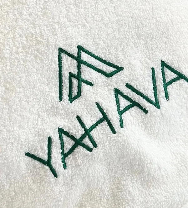 Toalha branca com o símbolo e o nome Yahava bordados em verde