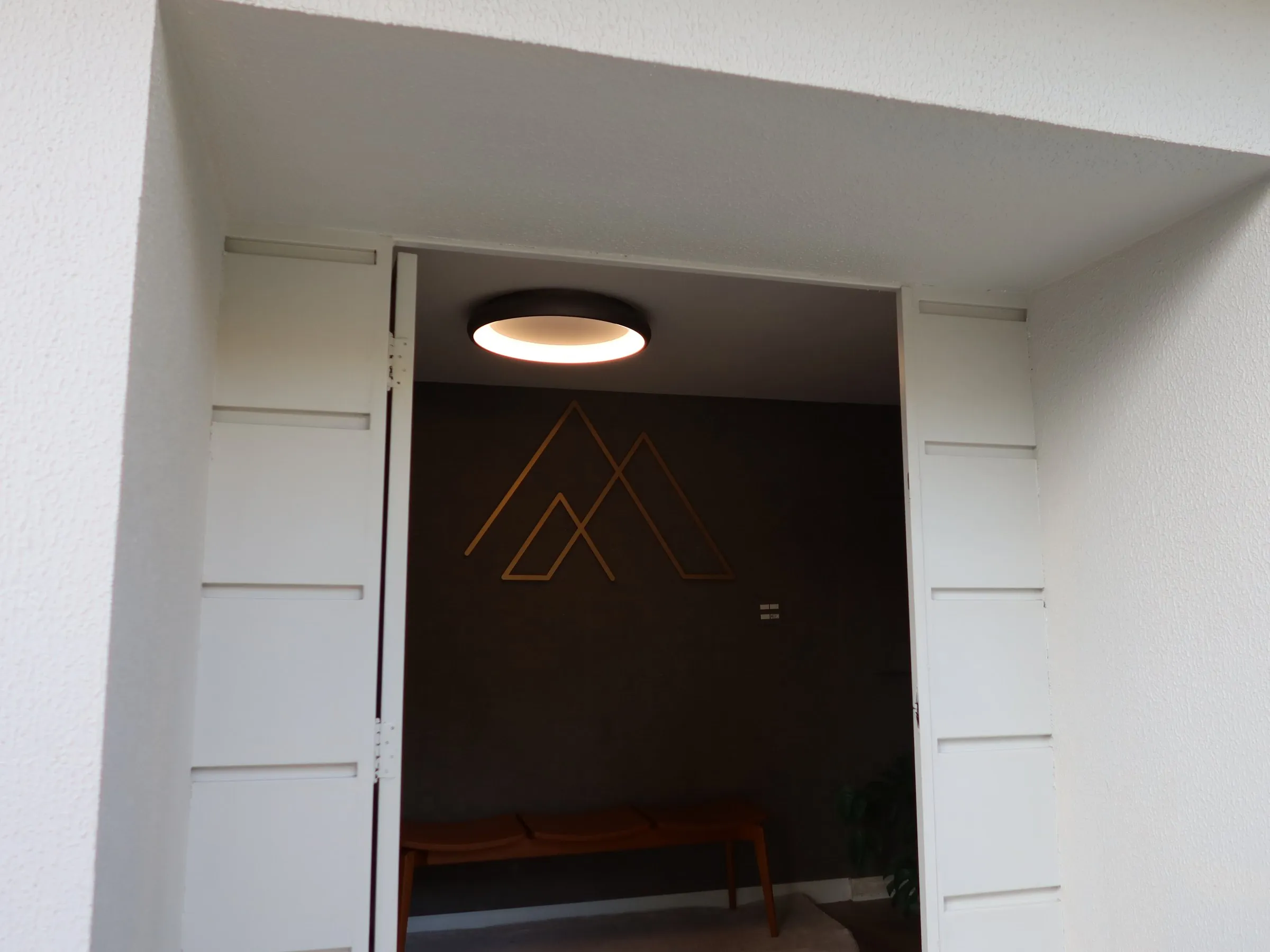 Porta de entrada da Casa Yahava aberta, com o símbolo dourado da marca na parede ao fundo
